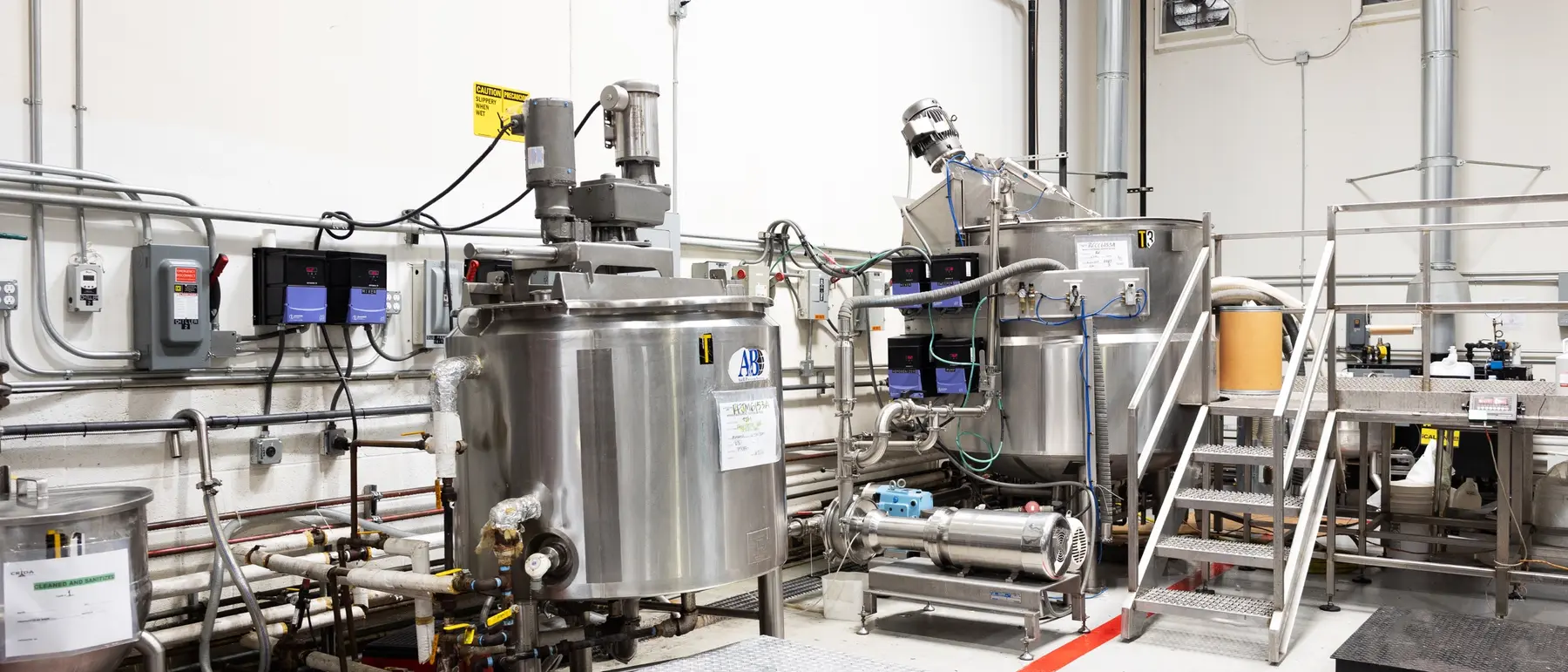 A stainless steel compounding tank tagged with a cleaned-and-sanitized batch record on CRIDA's floor
