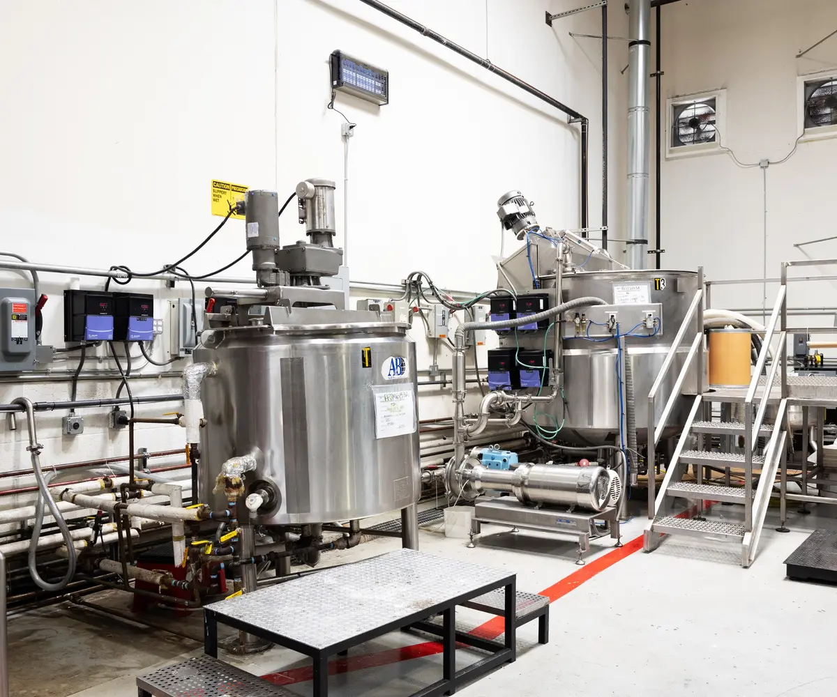 A stainless steel compounding tank on CRIDA's floor, tagged with a cleaned-and-sanitized batch record