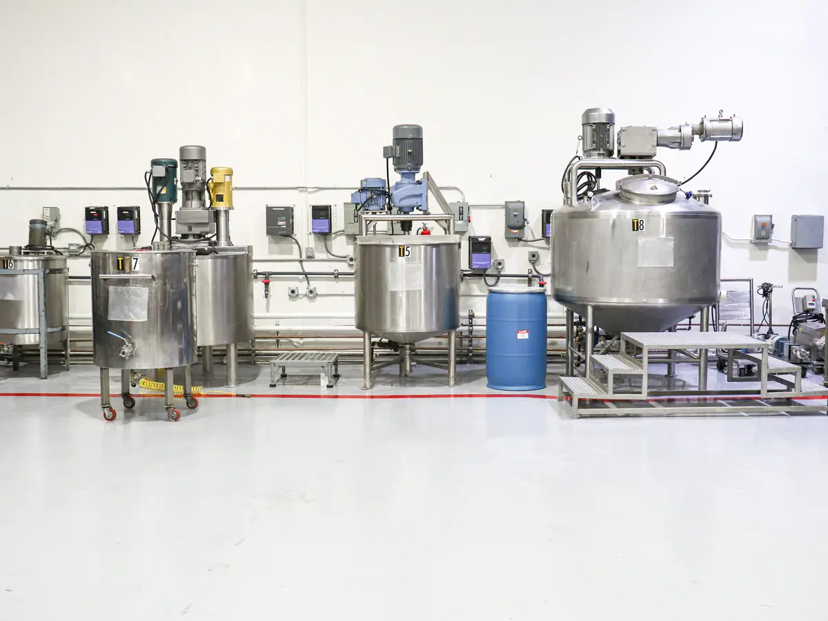 A row of stainless steel compounding tanks and mixers, labeled T5 through T8